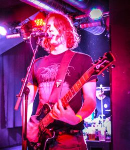 Till Steinberger performing live with guitar on stage in Vienna